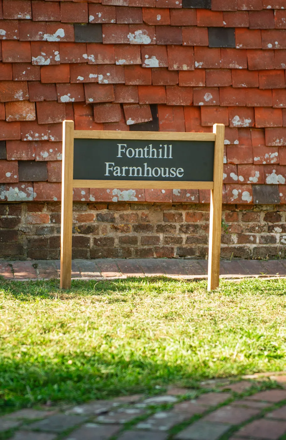 A dark sign with white lettering reading Fonthill Farmhouse on an oak frame in front of the tile-hung farmhouse wall